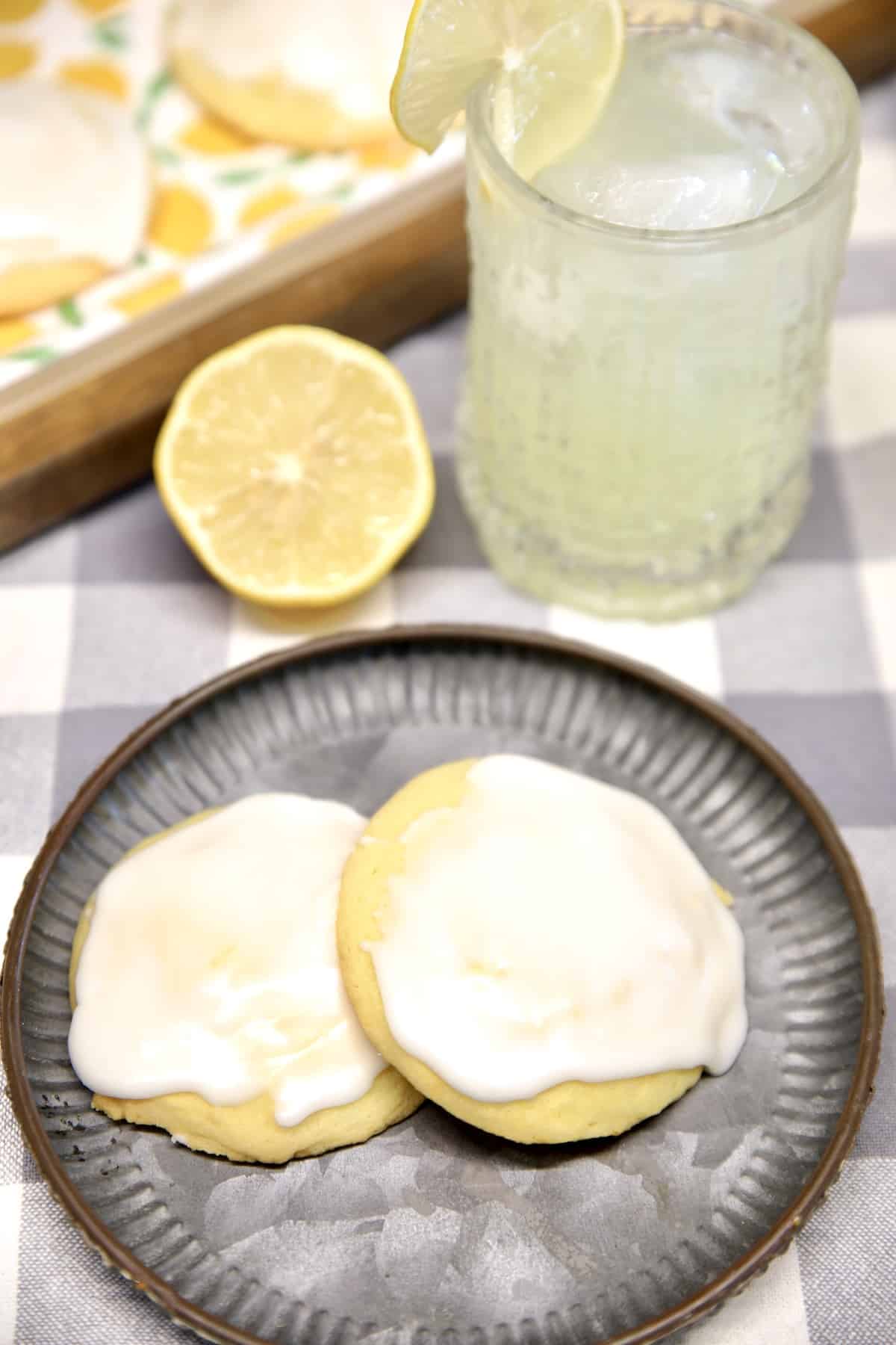 2 Lemon butter cookies on a plate, half of a lemon, glass of lemonade.