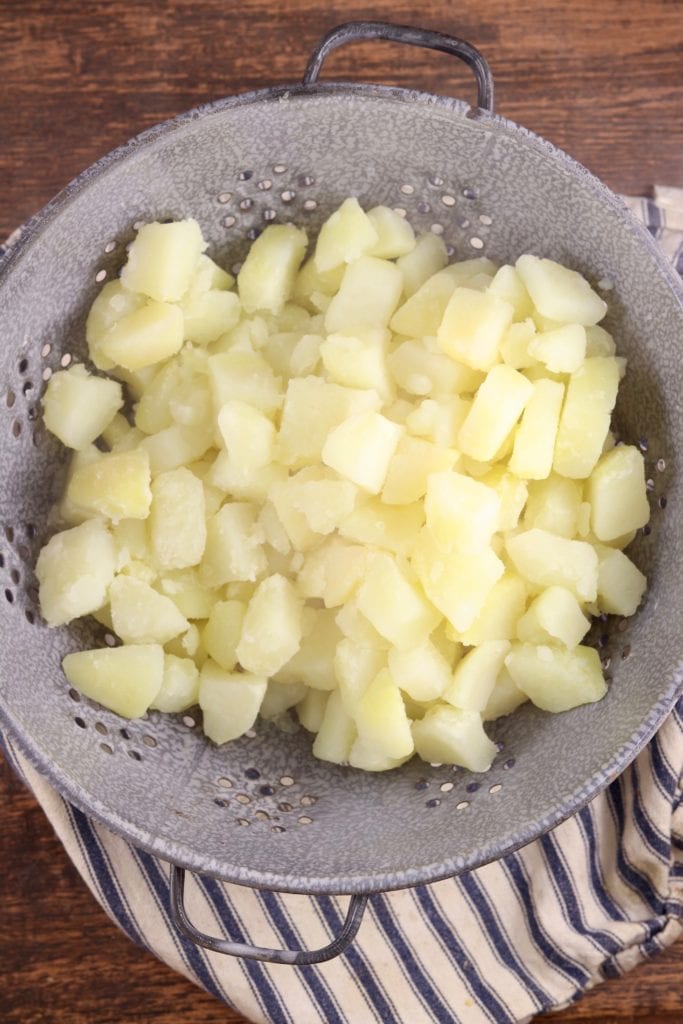 Boiled potato chunks draining in a gray colander
