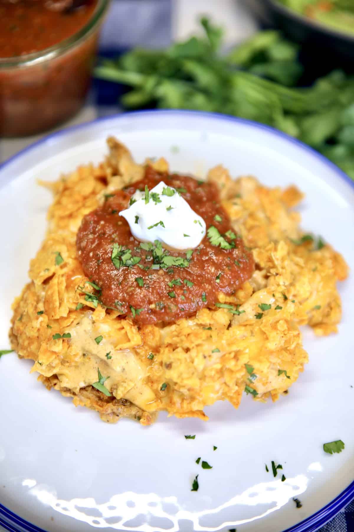 Doritos chicken casserole on a plate with sour cream and salsa.