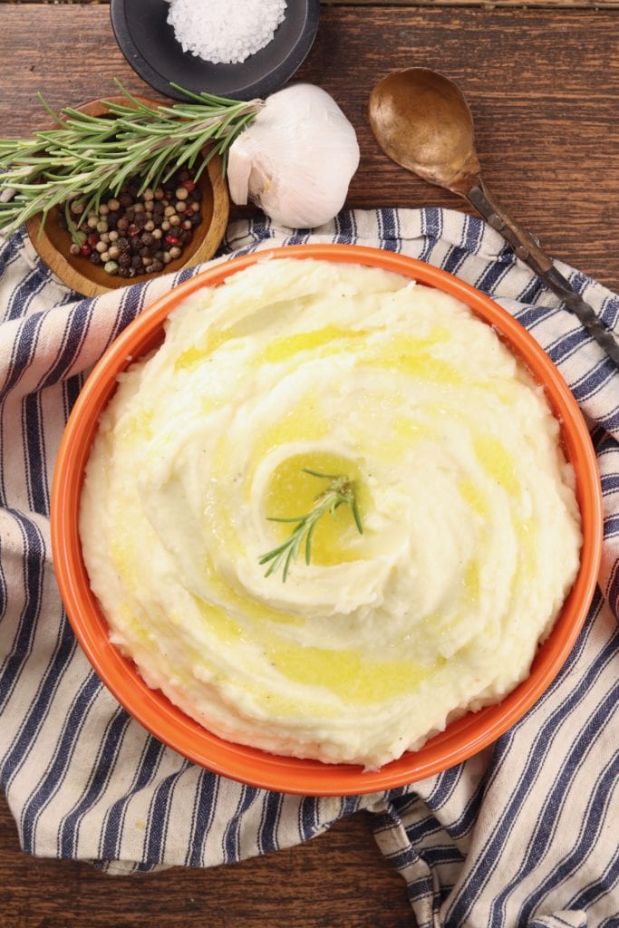 Garlic Mashed Potatoes in an orange serving bowl on a striped towel