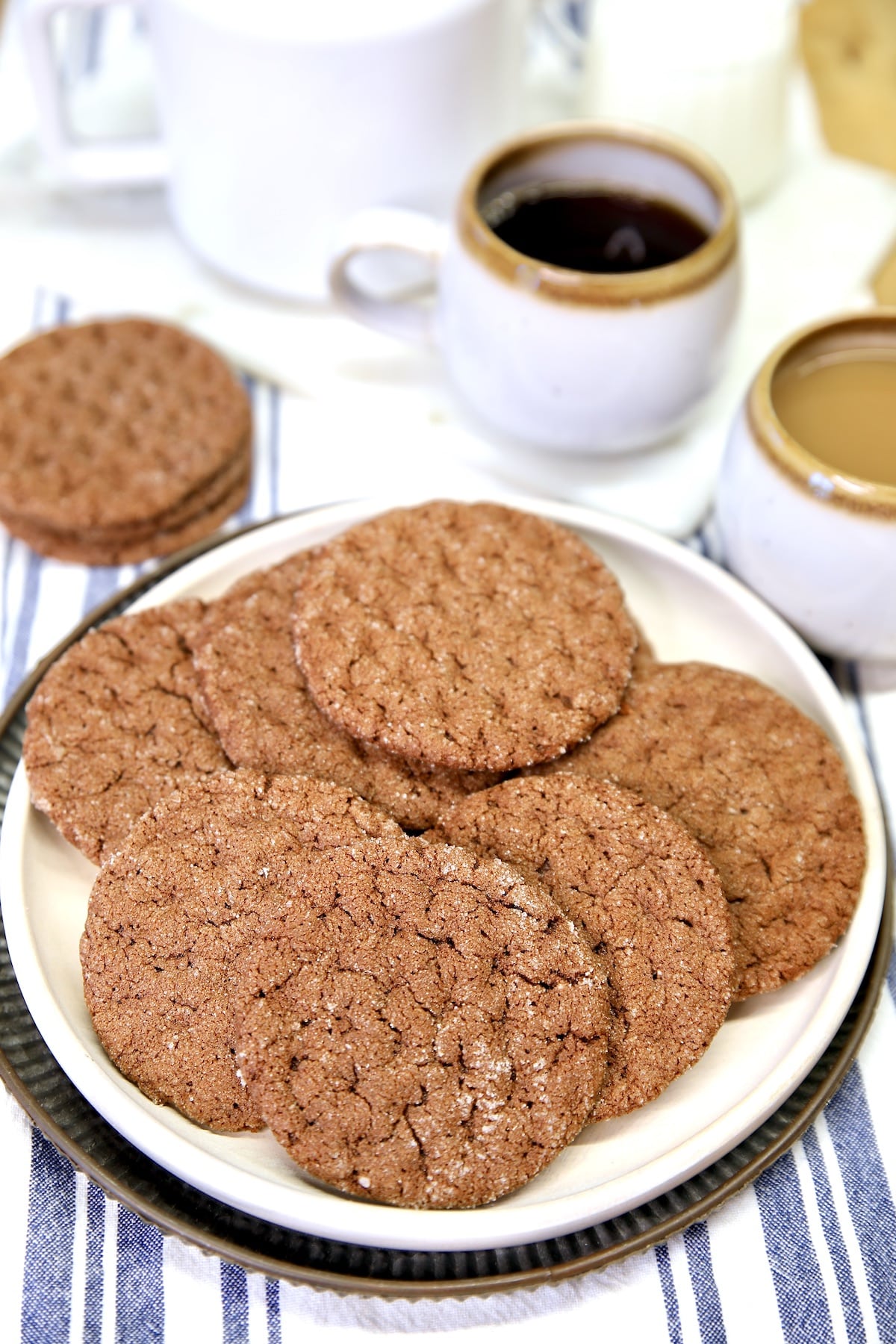 Plate of chocolate cookies with coffee cups.