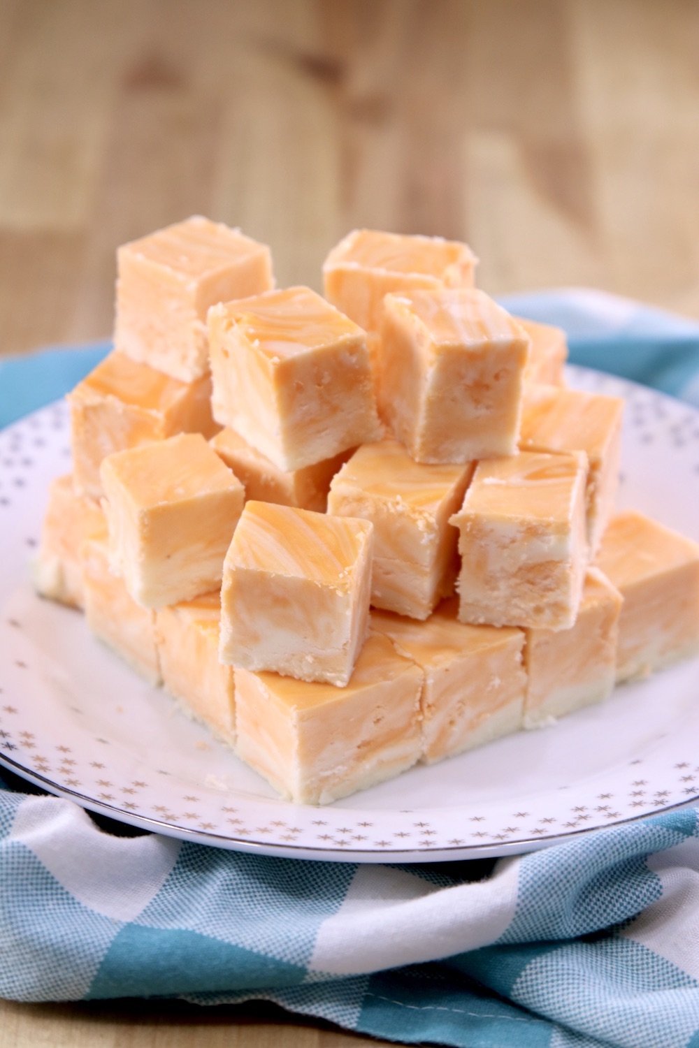 Squares of orange cream marble fudge stacked on a plate with blue and white check napkin