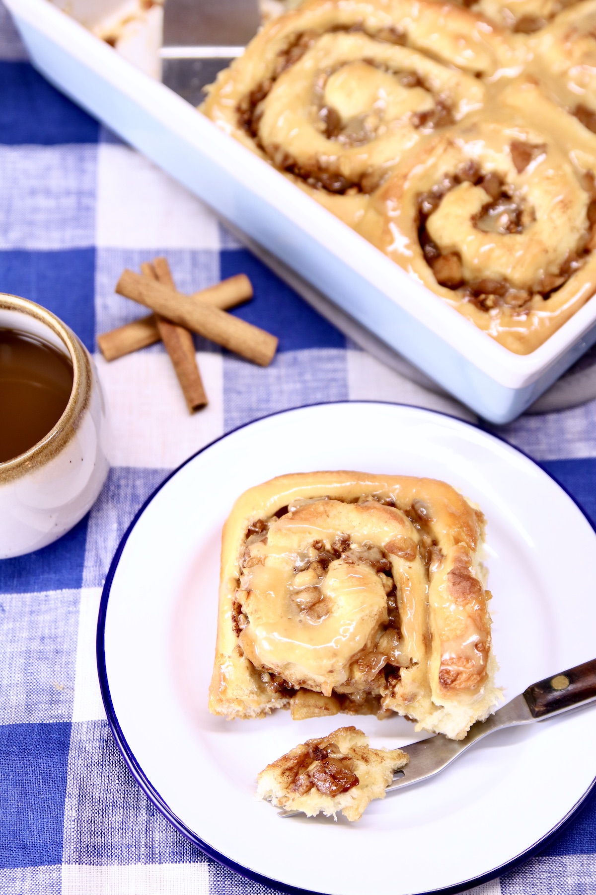 apple cinnamon roll on a plate with fork, pan of rolls