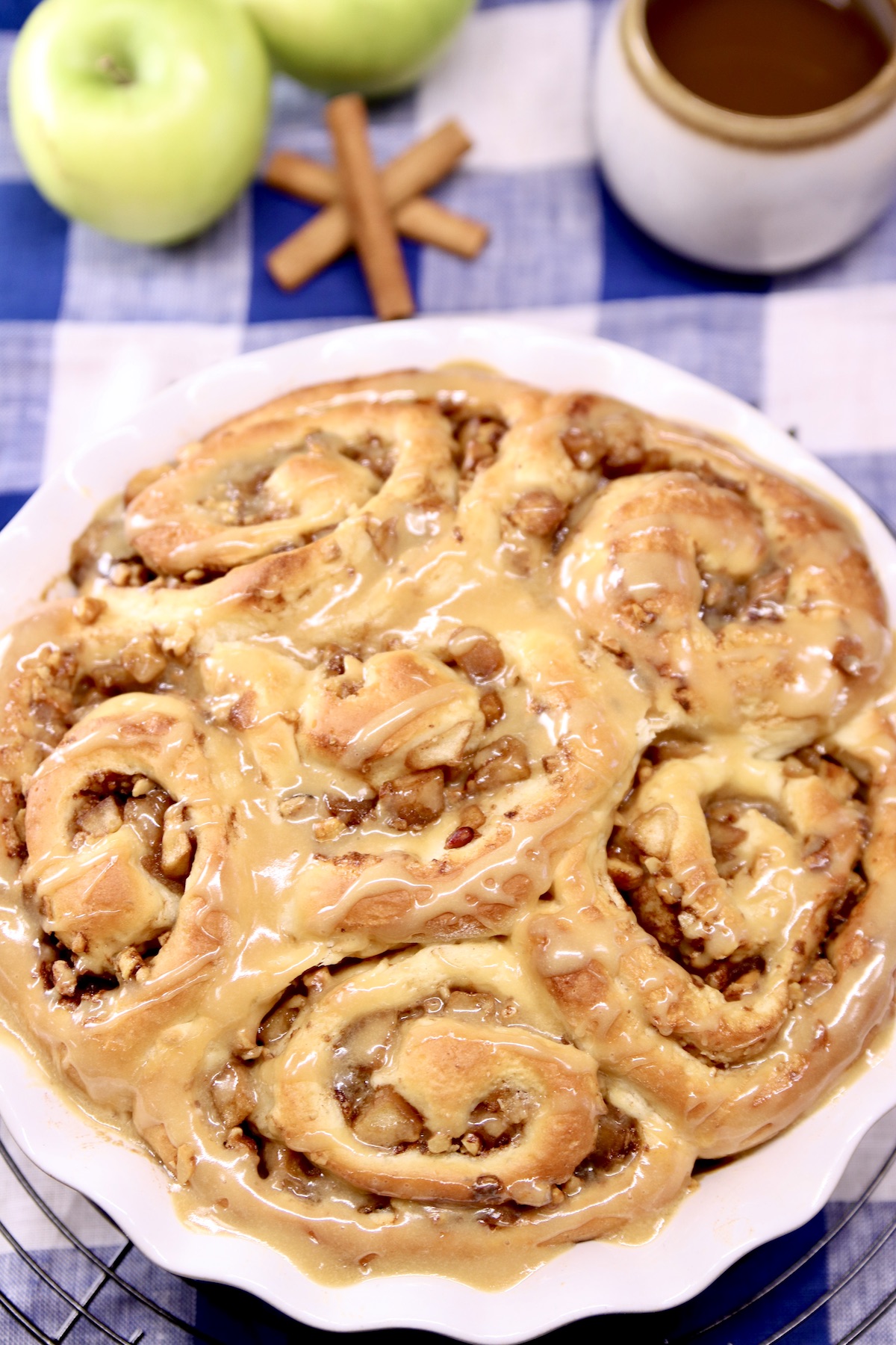 cinnamon rolls in a pie plate, apples, cinnamon sticks and cup of coffee in background