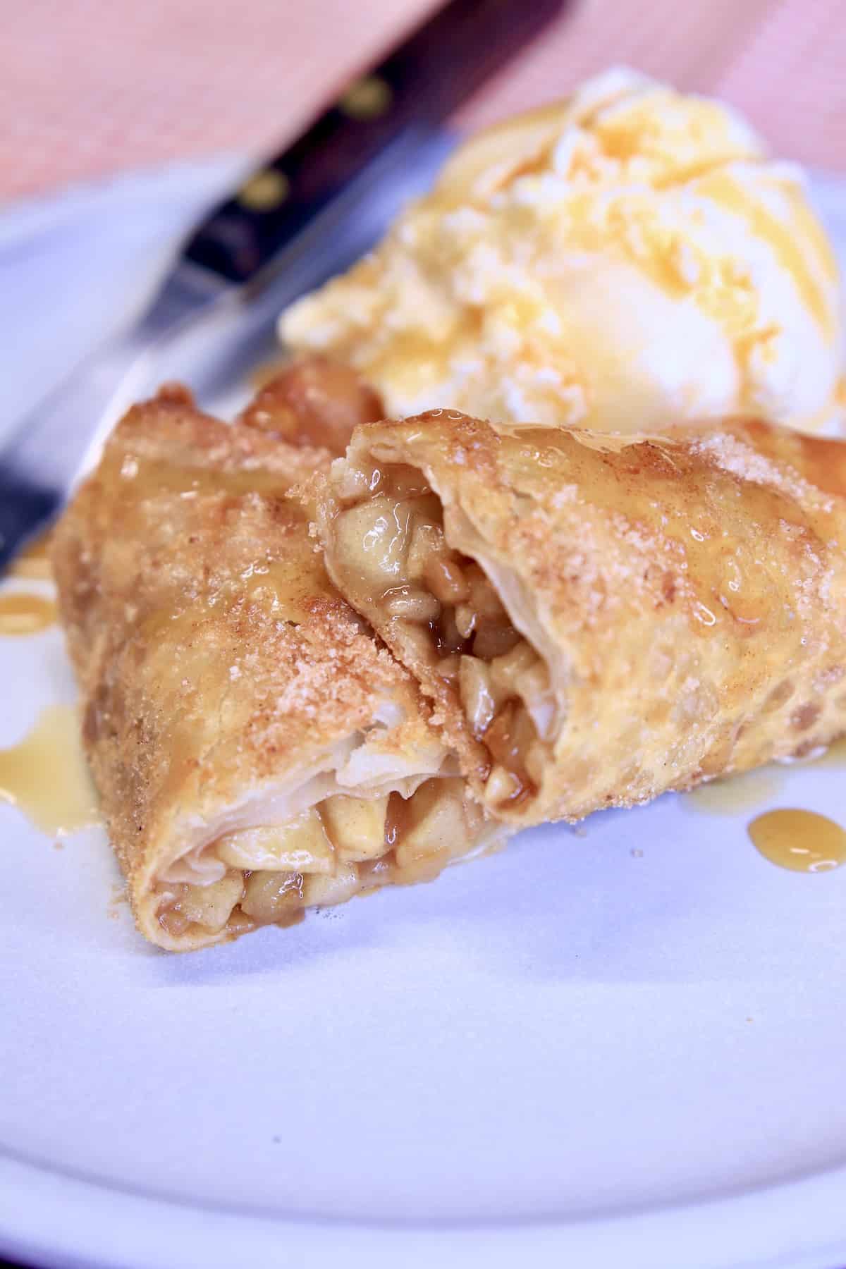 Apple filled egg roll, sliced on a plate with ice cream.
