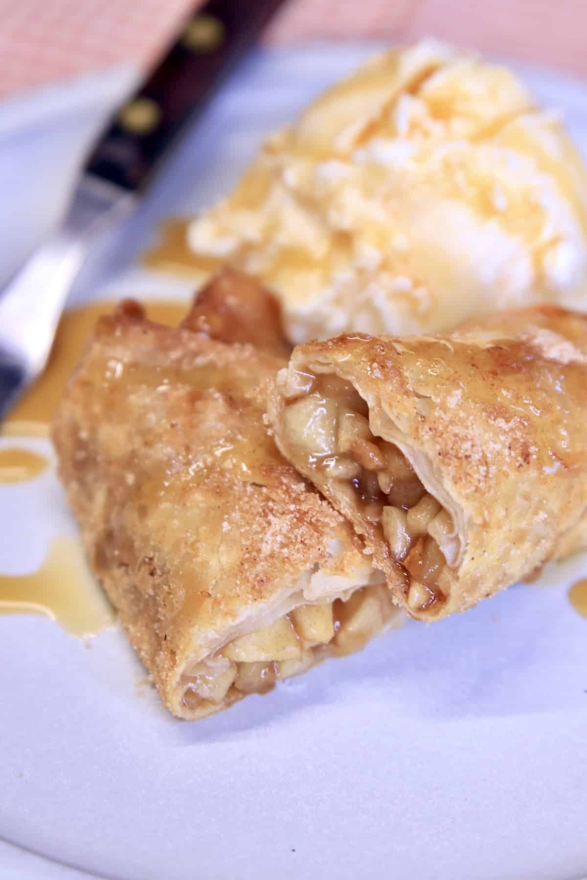 Apple Pie Egg Roll cut in half on a plate with vanilla ice cream and caramel sauce.