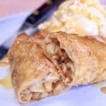 Apple Pie Egg Roll, cut in half, on a plate with vanilla ice cream and caramel sauce.