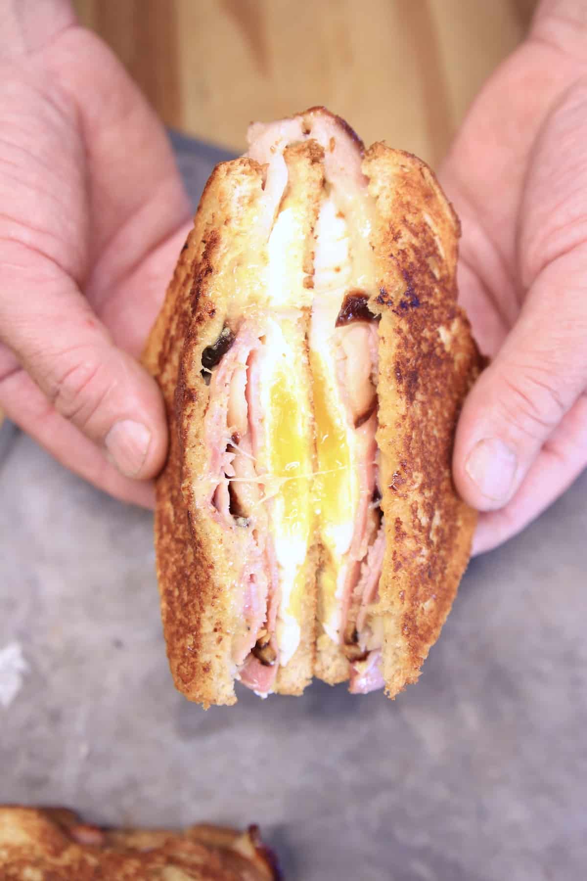 Hot ham, egg and cheese sandwich, cut in half, held in hands.