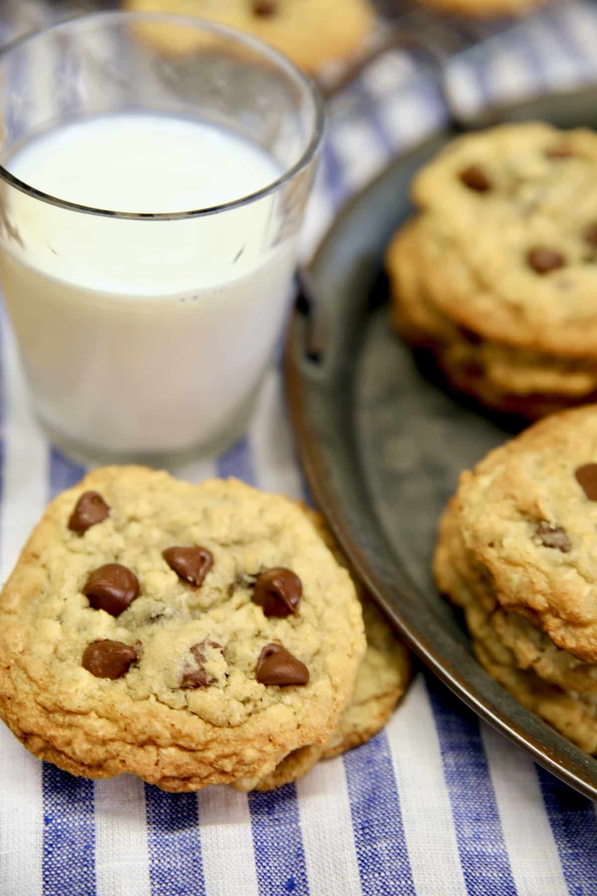 Cookies stacked in front of milk glass beside platter of cookies.