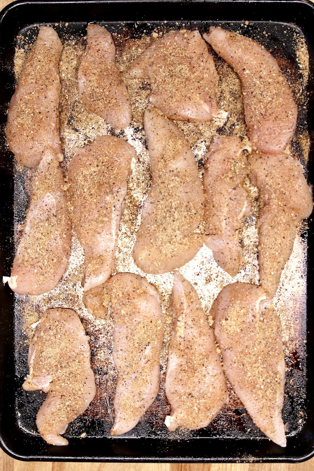 Chicken tenders with seasonings for grilling on a sheet pan