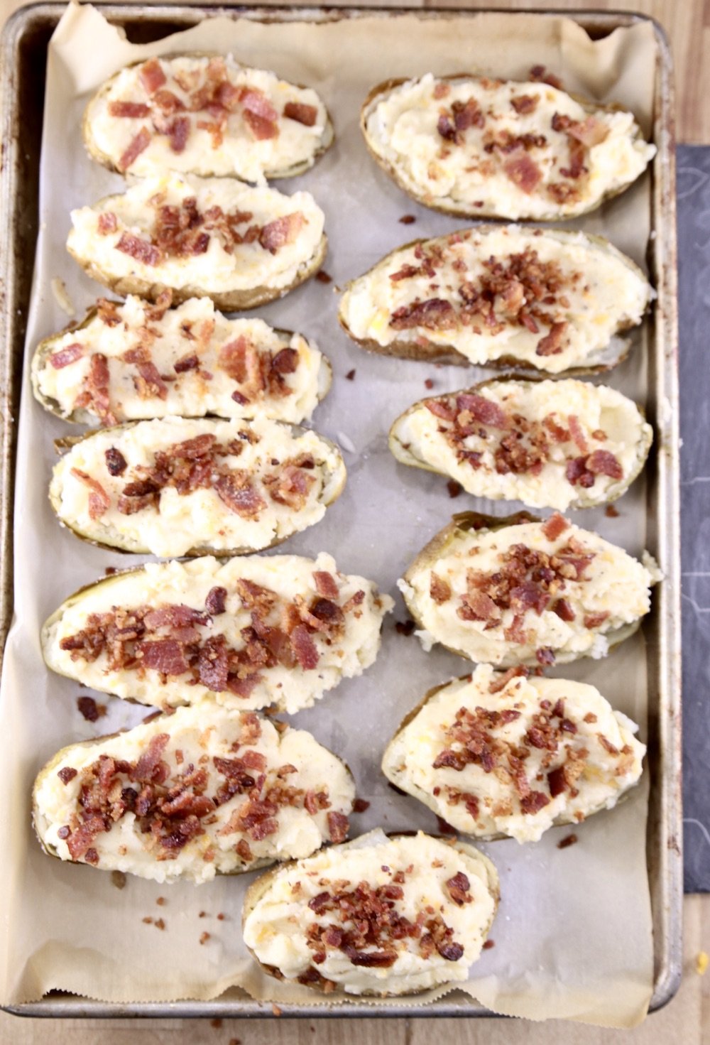 Half Baked Potatoes filled with potato and cheese mixture topped with bacon on a baking sheet