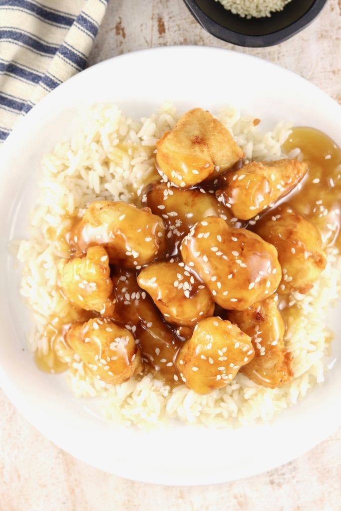 Overhead of sesame chicken served over rice on a white plate