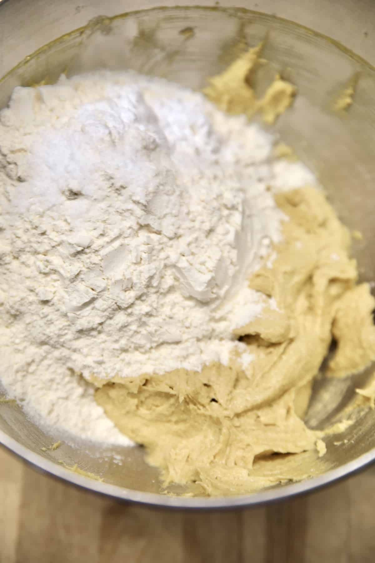Adding flour to cookie dough in a mixer bowl.