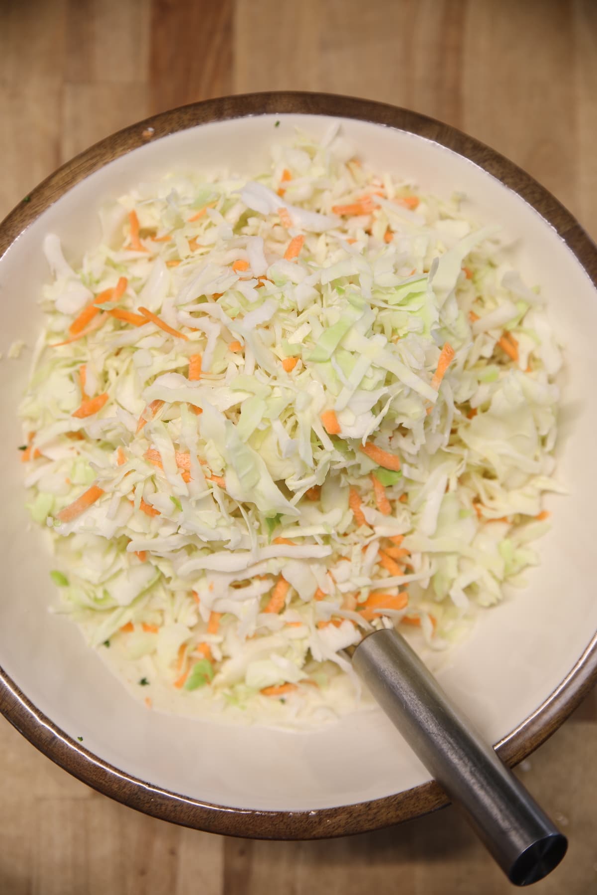 Bowl of shredded cabbage and carrots with a whisk.