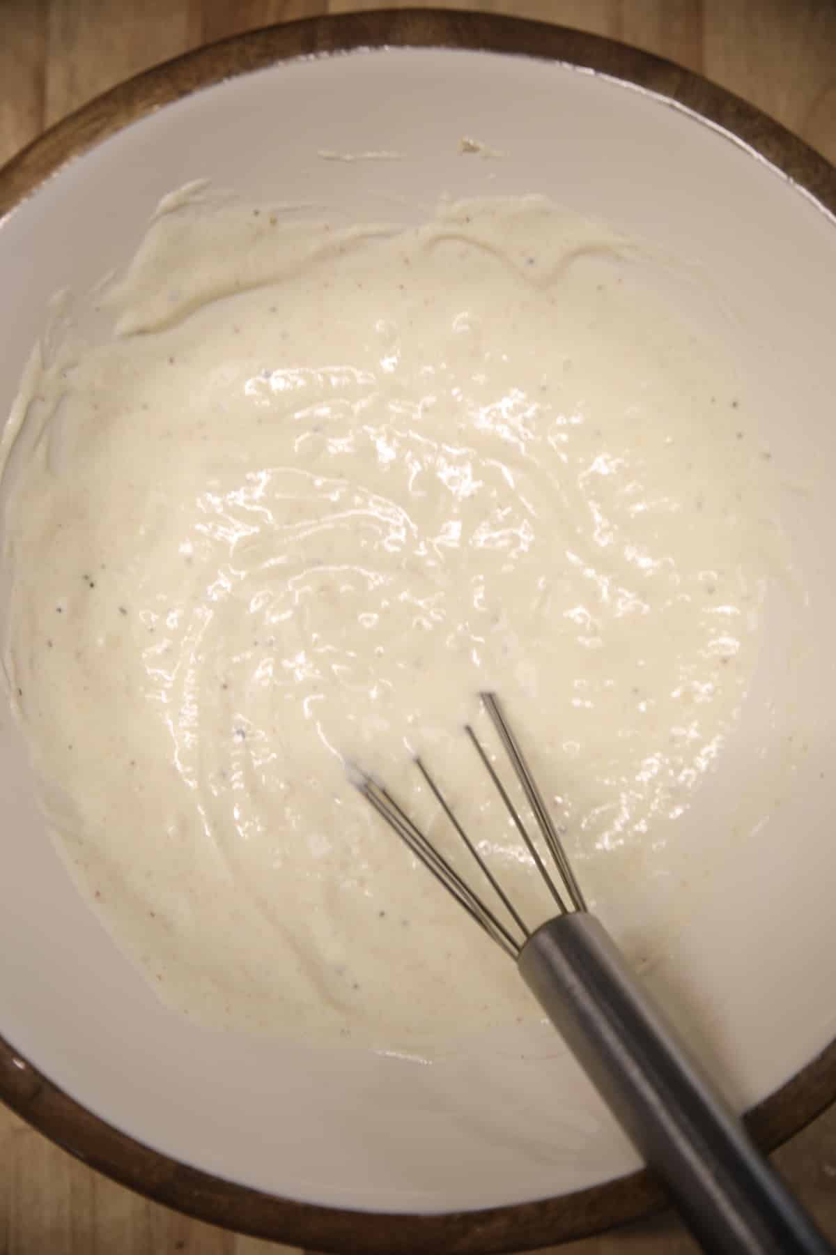 Creamy slaw dressing in a bowl with whisk.