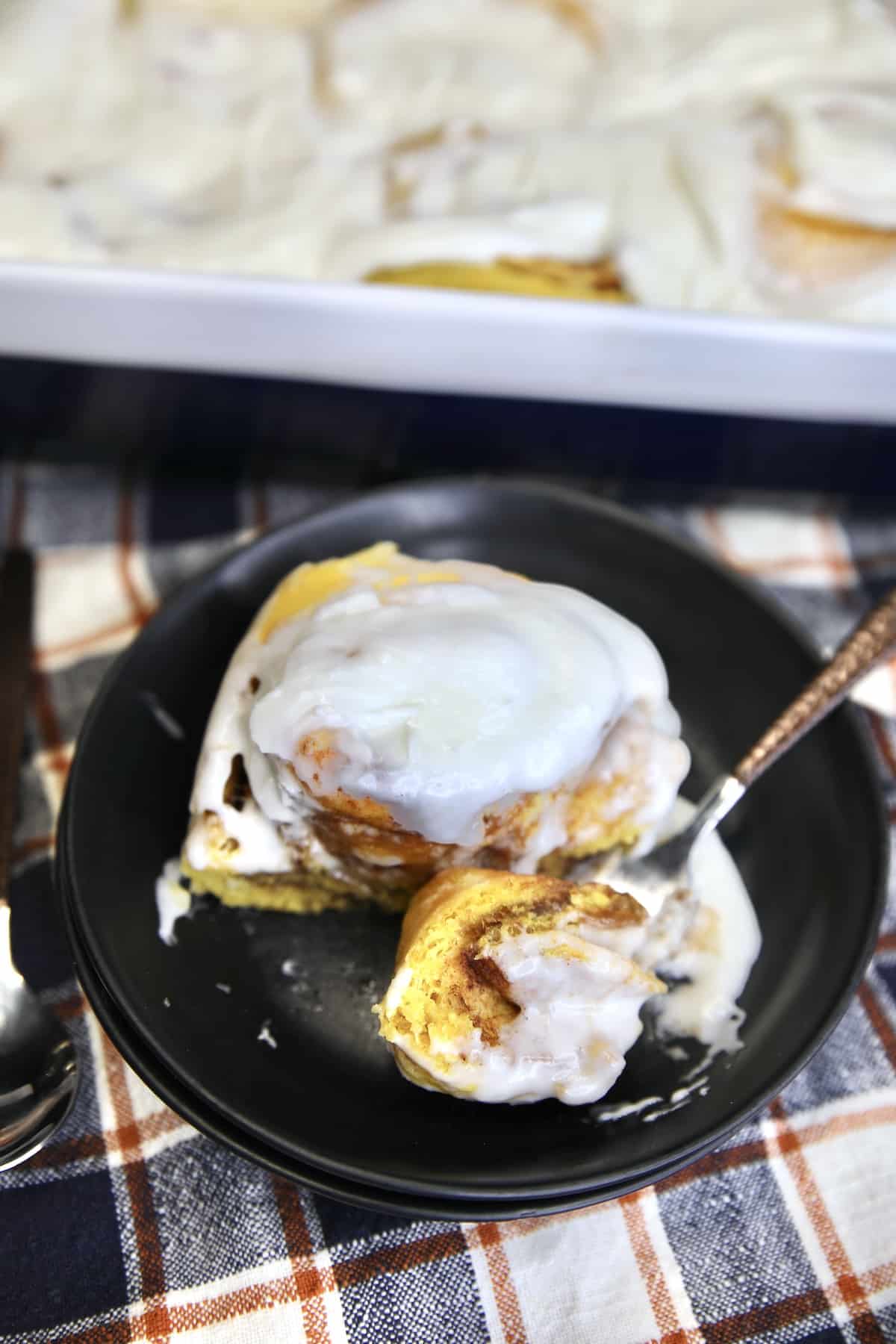 Pumpkin cinnamon roll in a dish with bite on a fork.