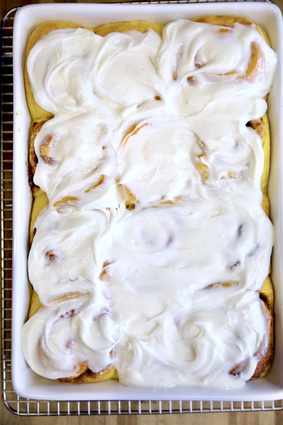 Pumpkin cinnamon rolls with cream cheese icing in a pan.