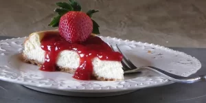 Strawberry Cheesecake topped with strawberry sauce and whole strawberry on plate with fork