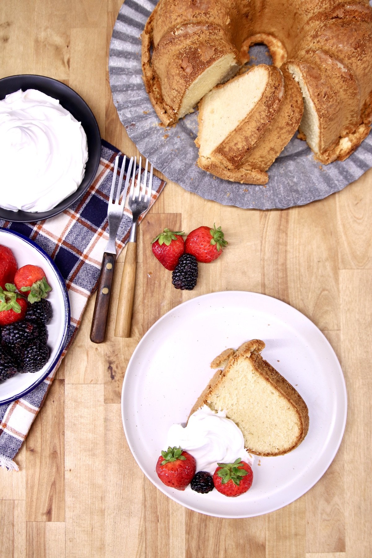 slice of pound cake with berries and whipped cream, cake on platter, bowls of whipped cream, berries
