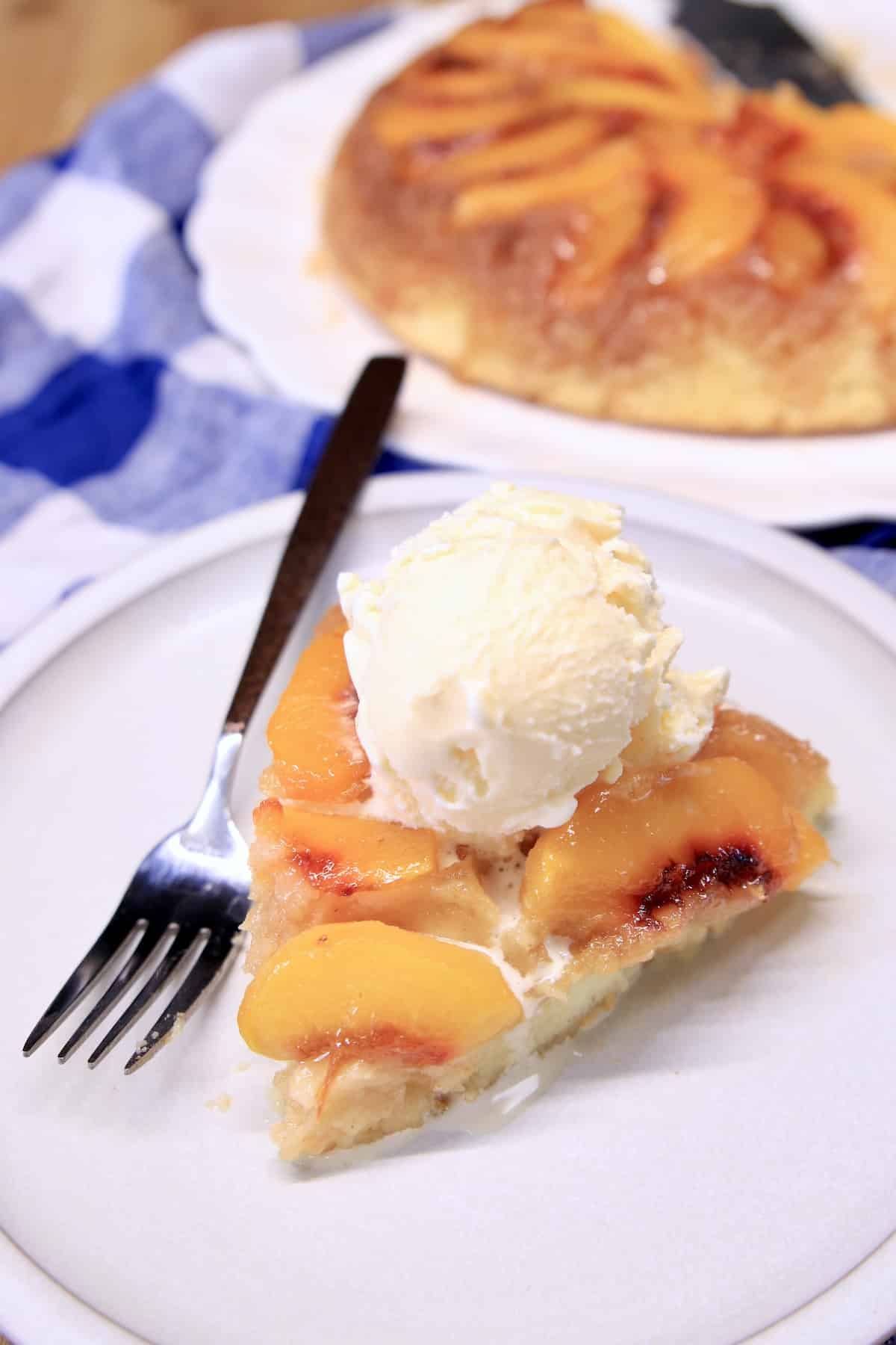 Slice of Peach Upside Down cake with vanilla ice cream on a plate with fork.
