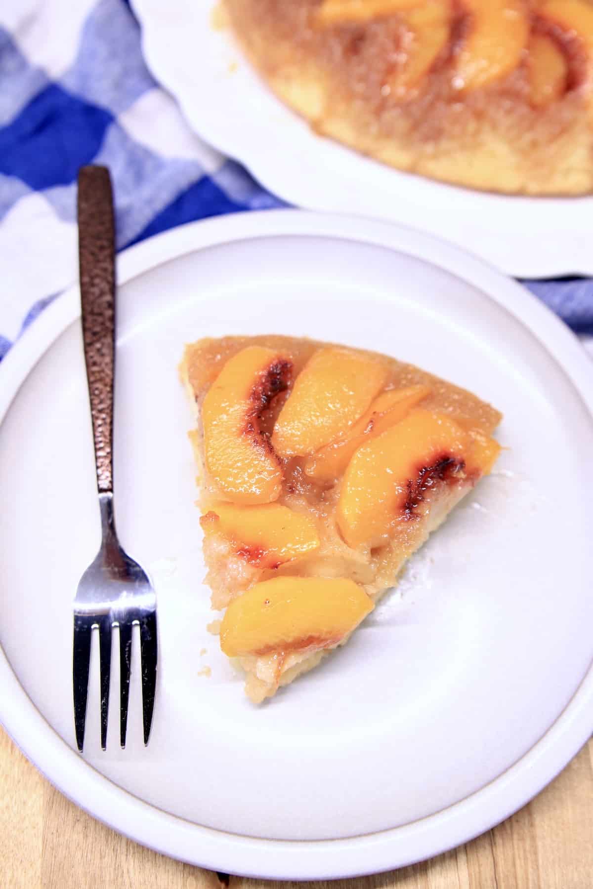 Slice of peach upside down cake on a white plate with fork.