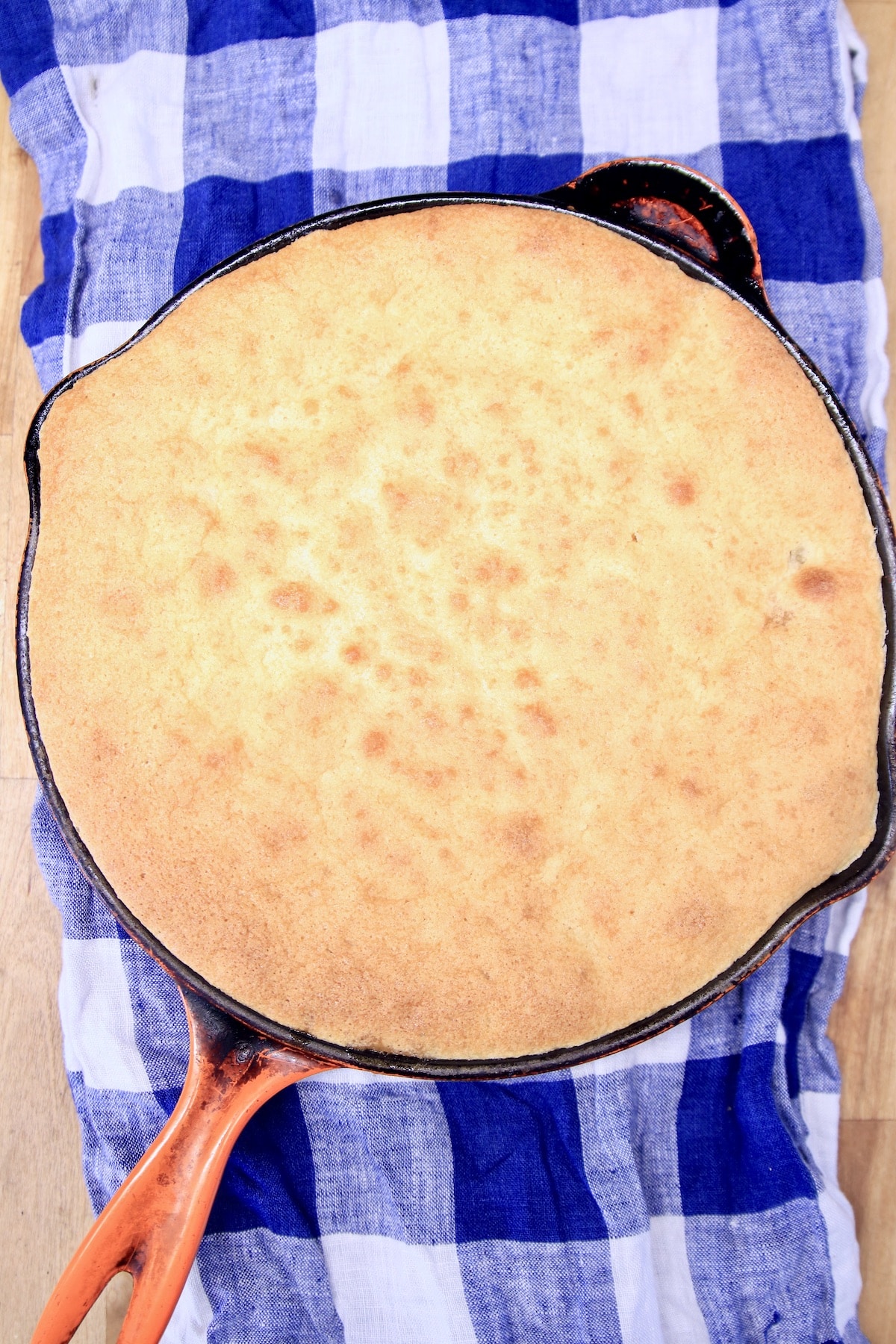 Skillet with baked cake on a blue and white checked cloth.