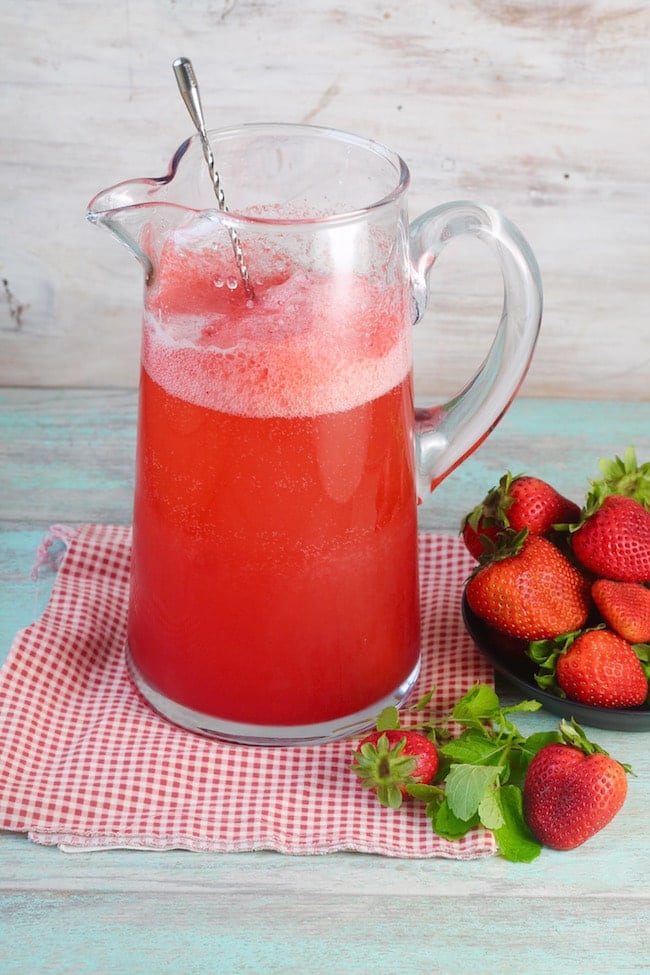 Pitcher of Strawberry Wine Punch and a bowl of fresh strawberries on a red check napkin