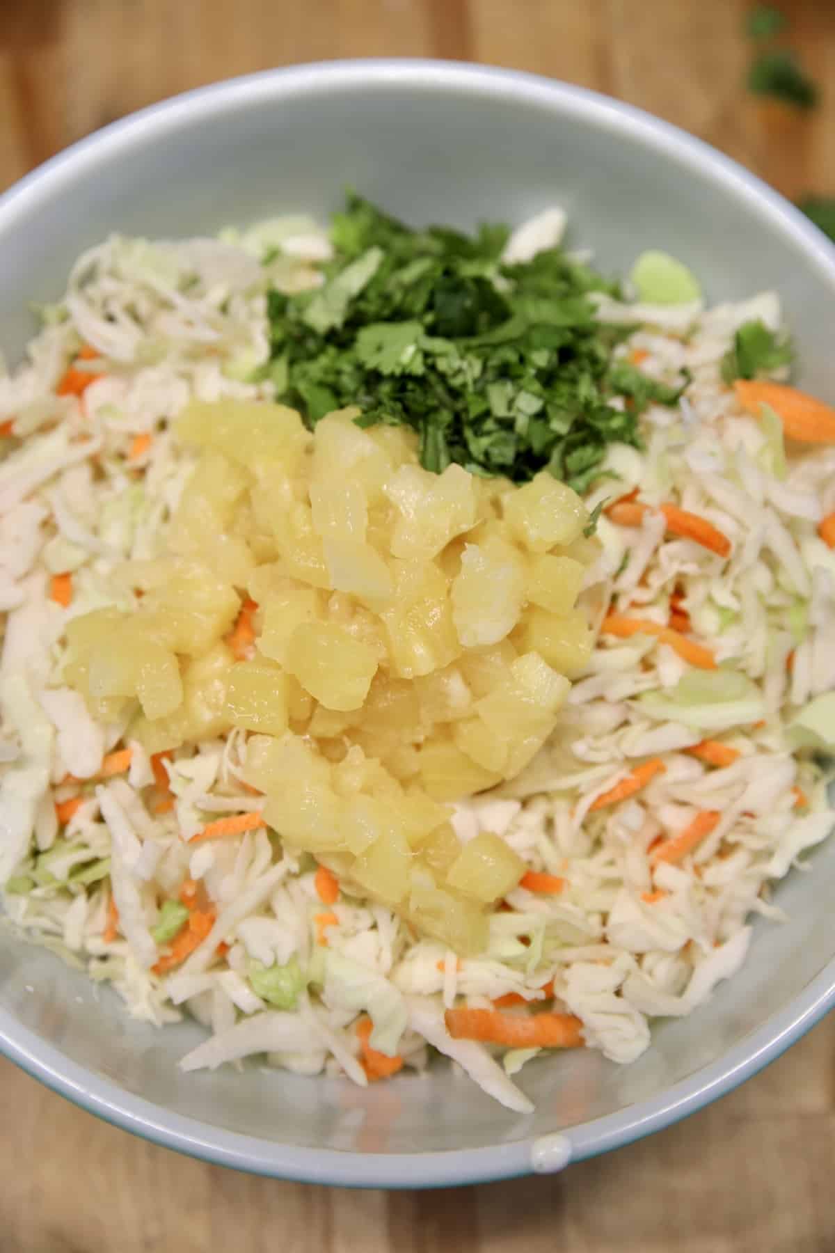 Bowl with shredded cabbage, carrots, pineapple and cilantro.