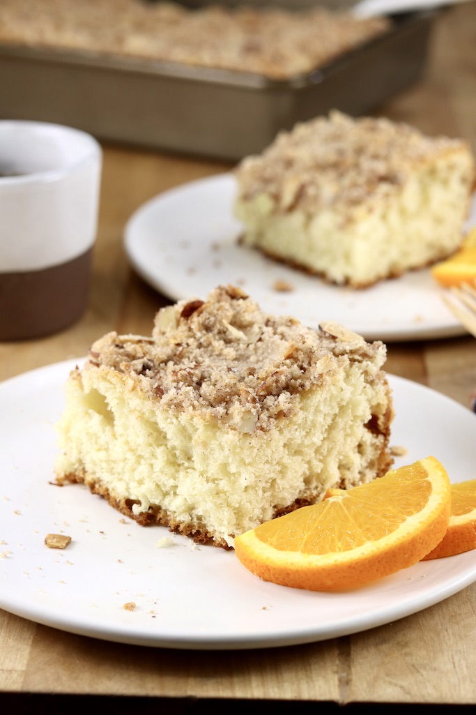 Slices of streusel coffee cake with slices of orange, coffee cup in back ground