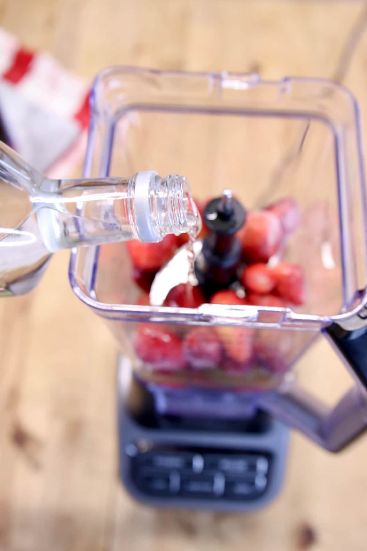 Pouring vodka into a blender with strawberries.