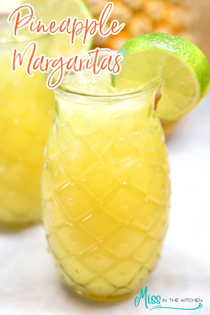 Pineapple Margaritas in tiki glass with lime wheel. Text overlay.