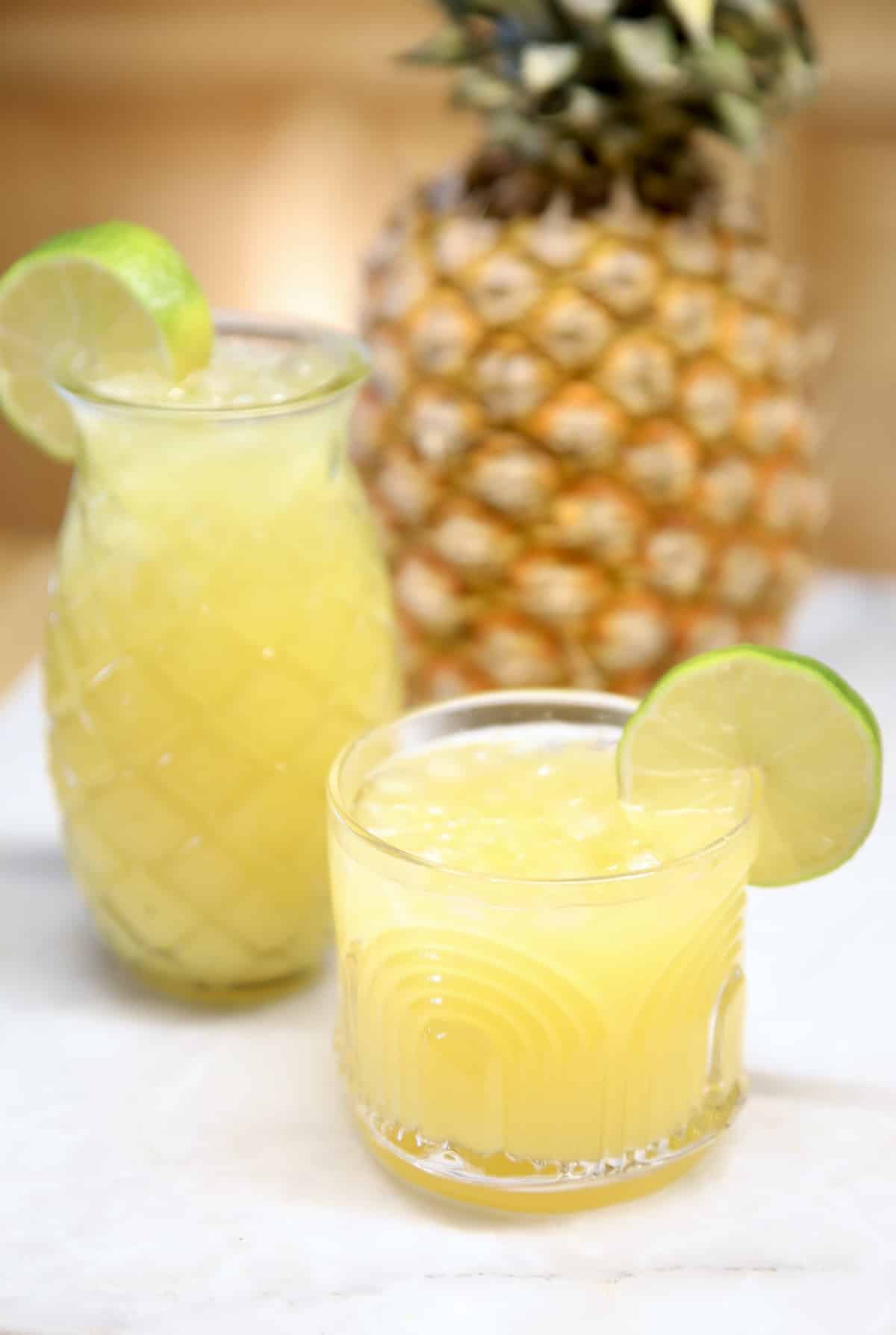 Pineapple Margaritas in a pineapple glass & tiki glass, pineapple in background.