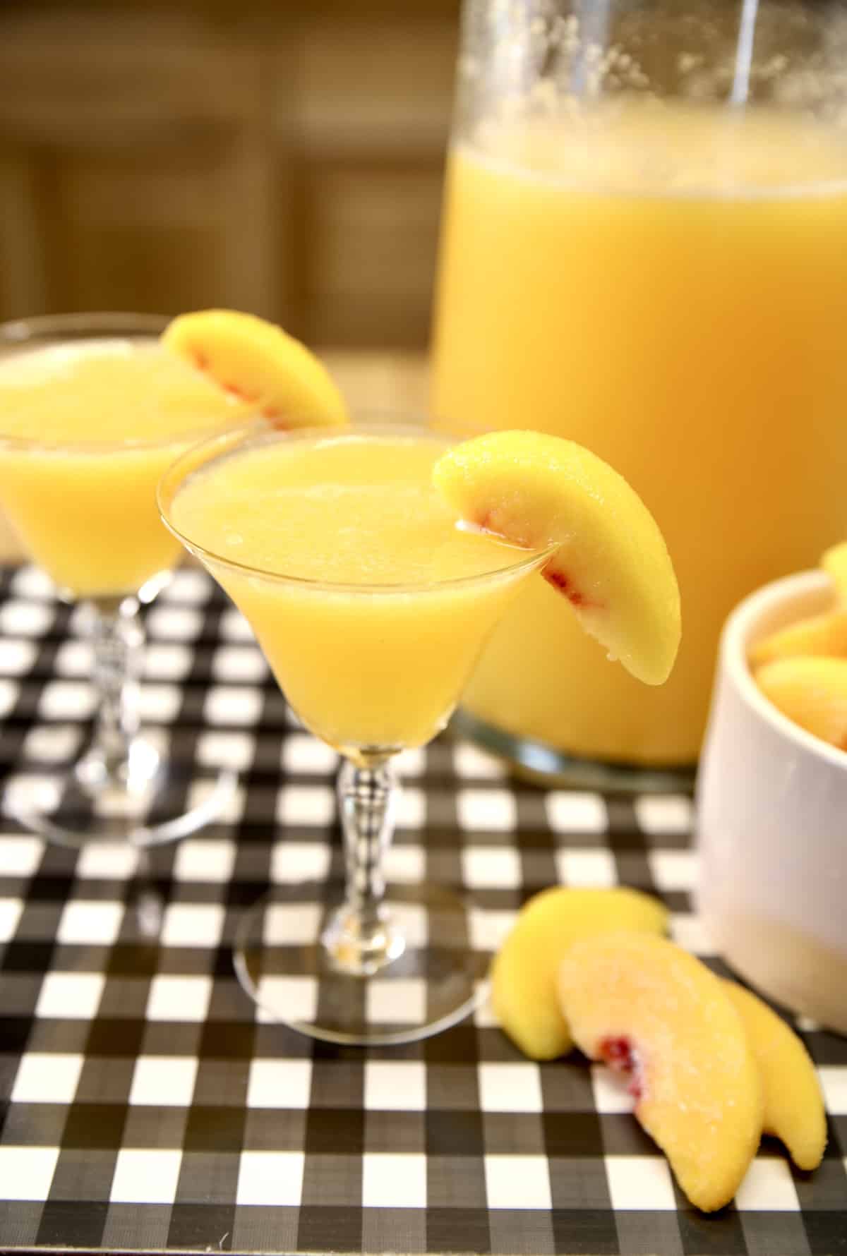2 glasses with peach cocktails, pitcher, sliced peaches.
