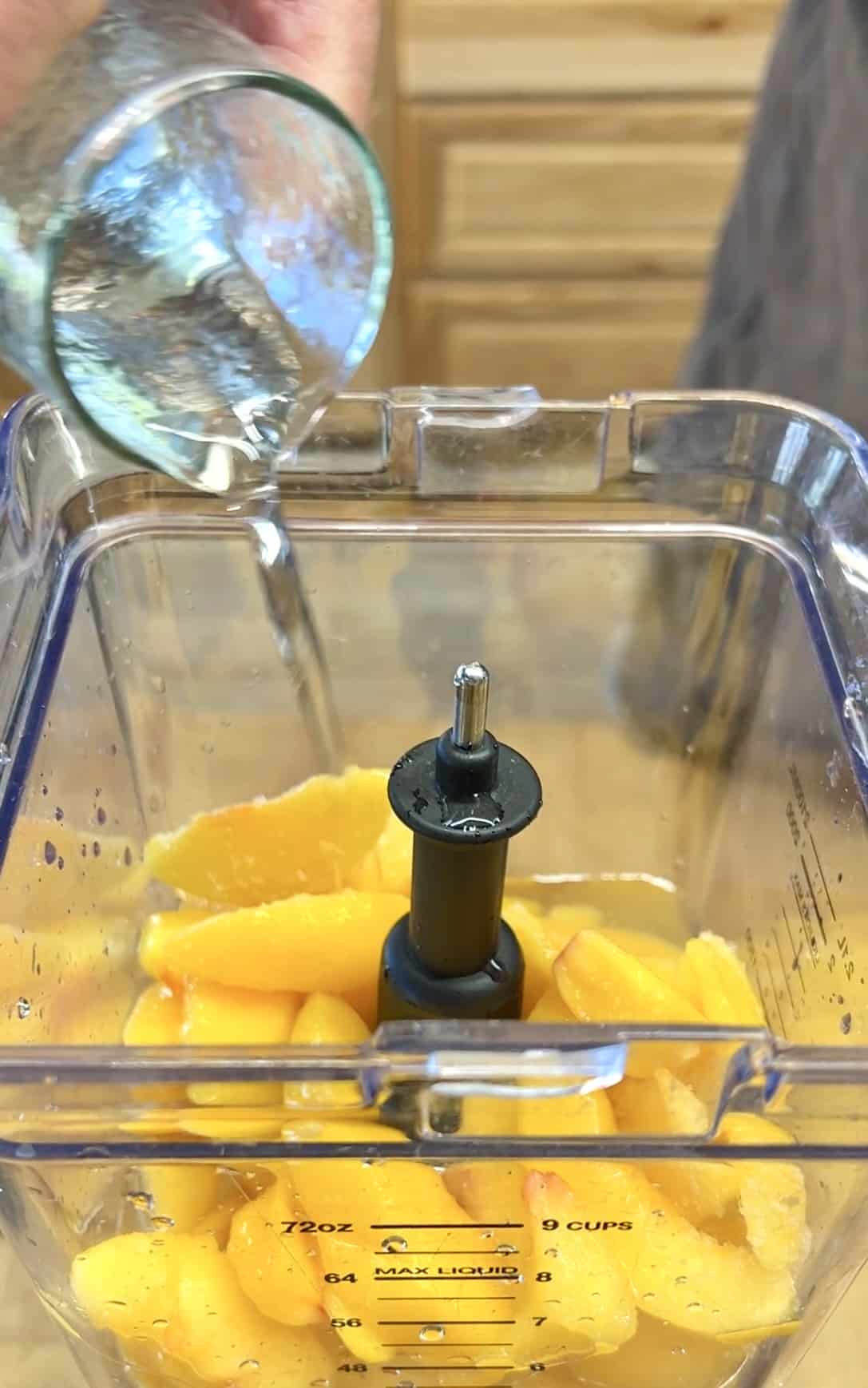 Pouring simple syrup into a blender with peaches.