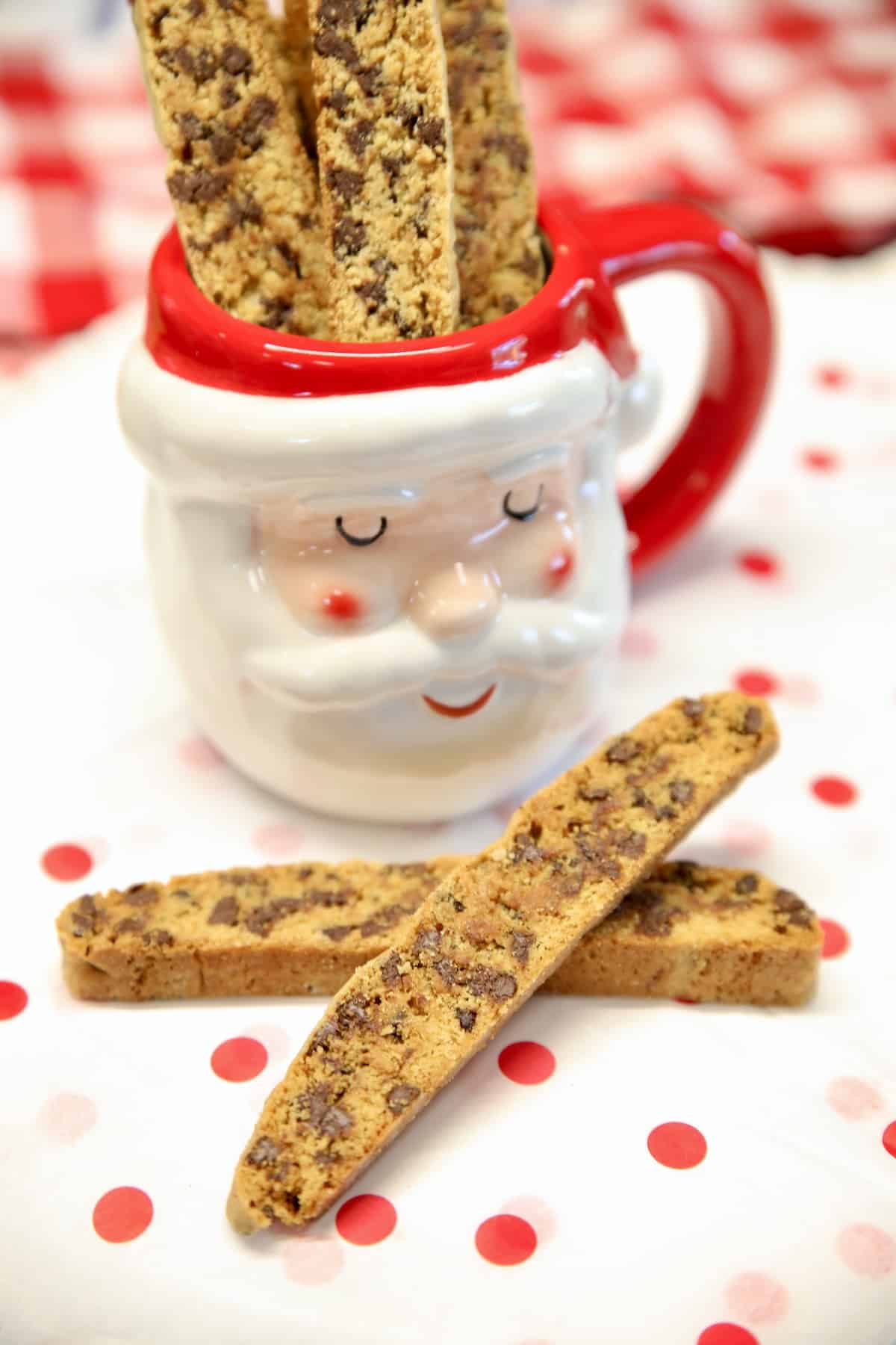 Santa mug with chocolate chip biscotti and 2 biscotti on a red dot cloth.