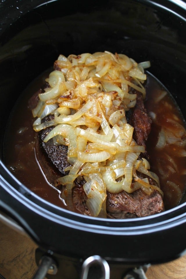 Beef pot roast in slow cooker topped with caramelized onions