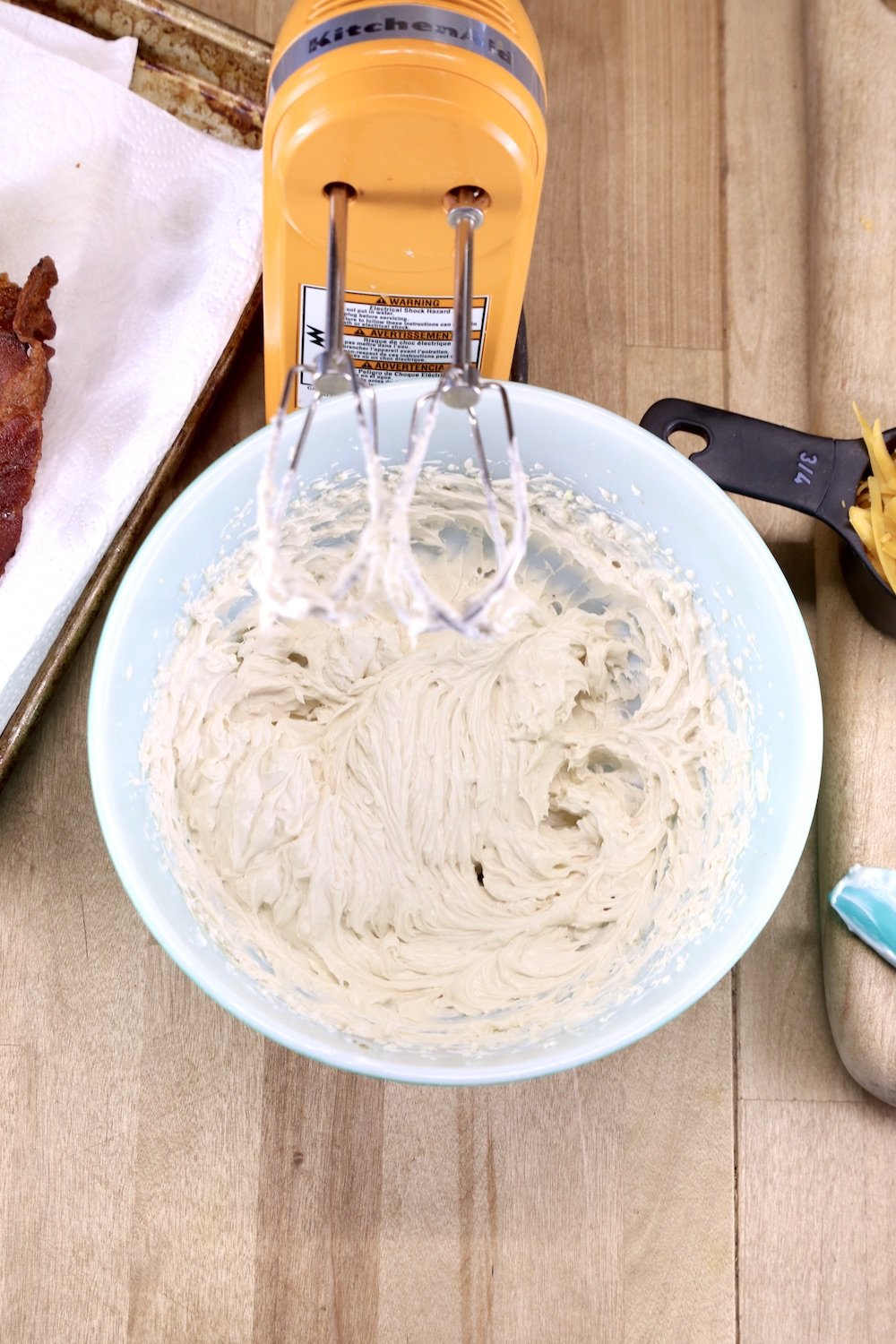 Cream cheese mixture whipped in a bowl until creamy, orange hand mixer with the bowl