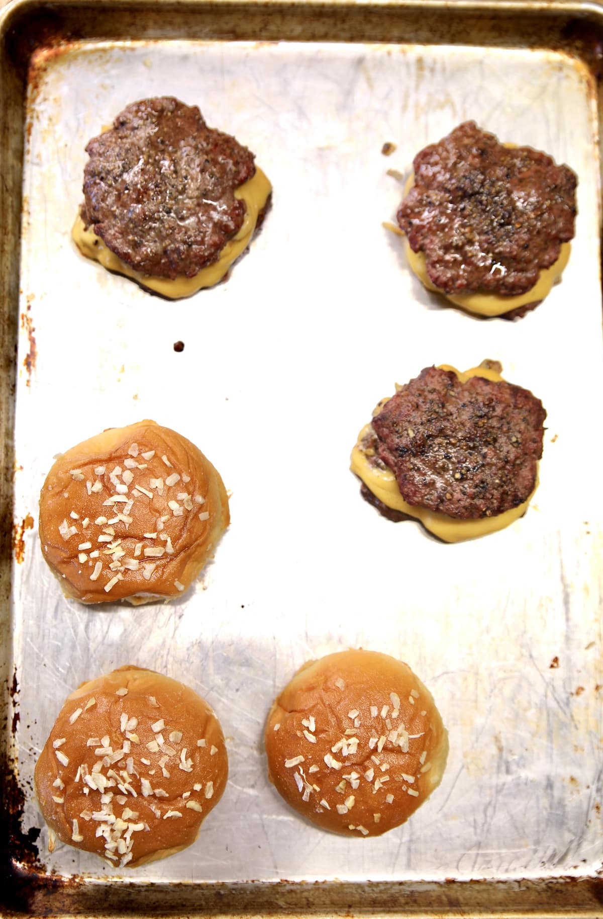 Sheet pan with grilled burgers, buns.