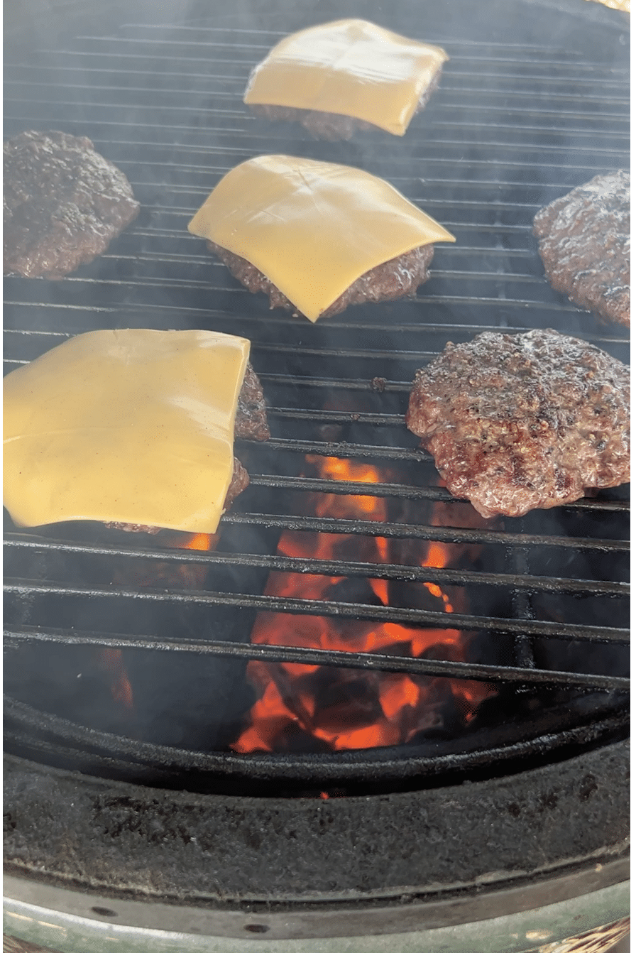 Burger patties on a grill, some topped with cheese.