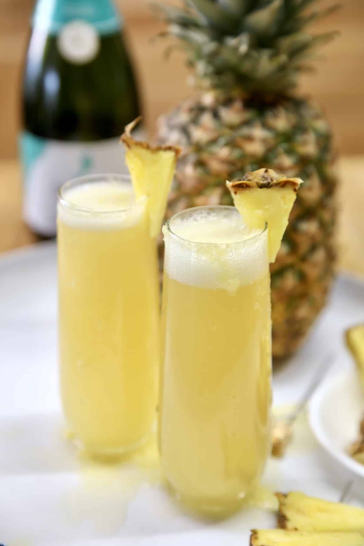 2 stemless champagne glasses with pineapple mimosas, pineapple garnish.