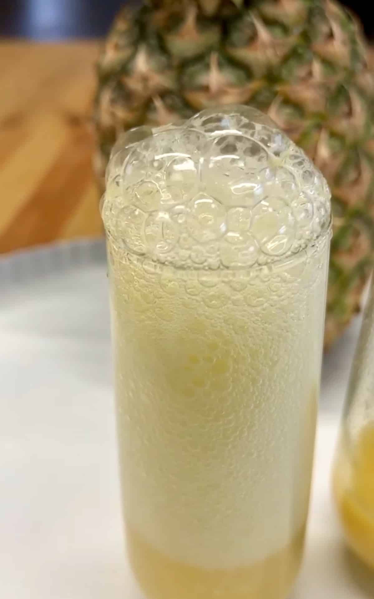 Pineapple mimosa with sparkling wine bubbling out the top of glass.