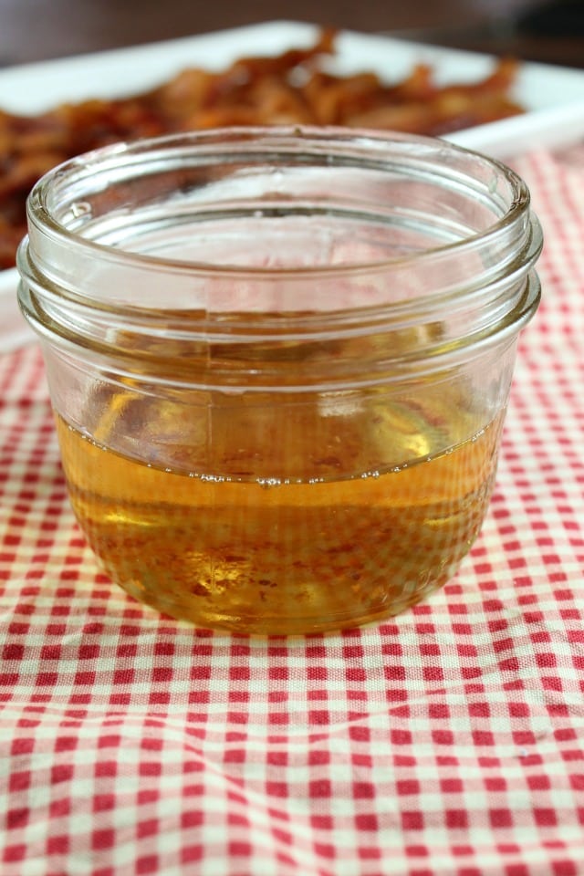 Bacon Drippings in a jar with bacon in the back ground, red gingham cloth under jar