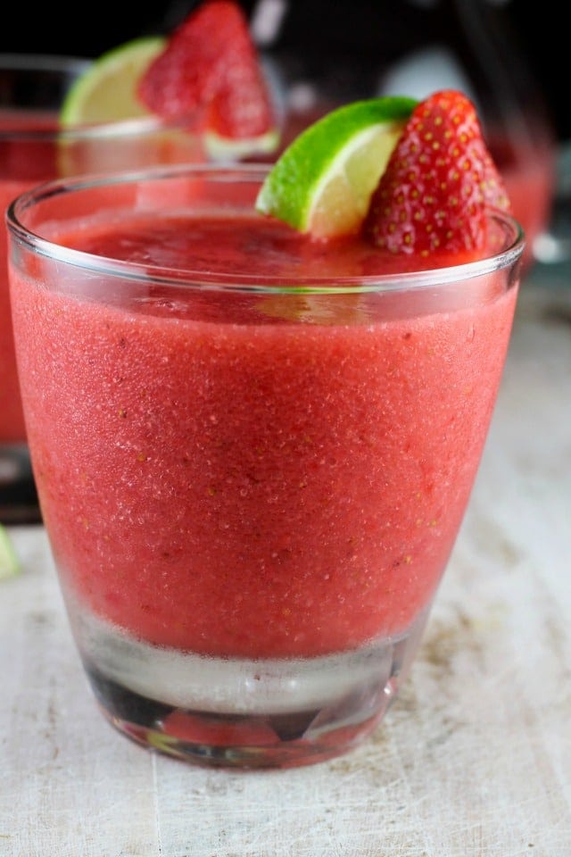 Frozen strawberry daiquiri in a glass with lime and strawberry garnish.