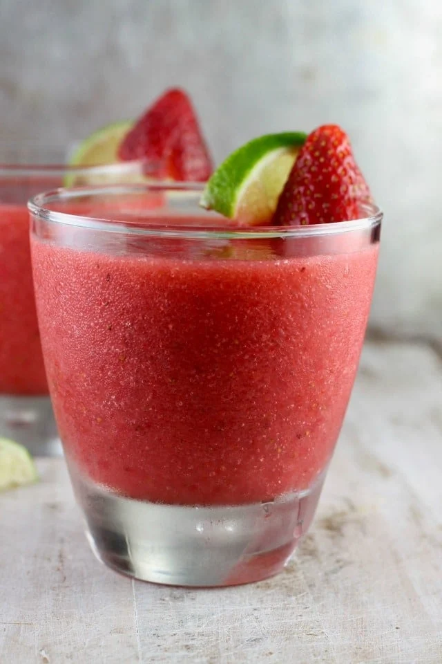 Strawberry daiquiri in a glass with lime and strawberry garnish.
