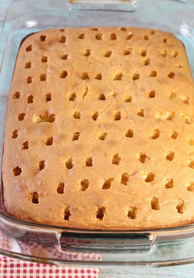 Baked yellow cake with holes poked all over in a glass baking dish