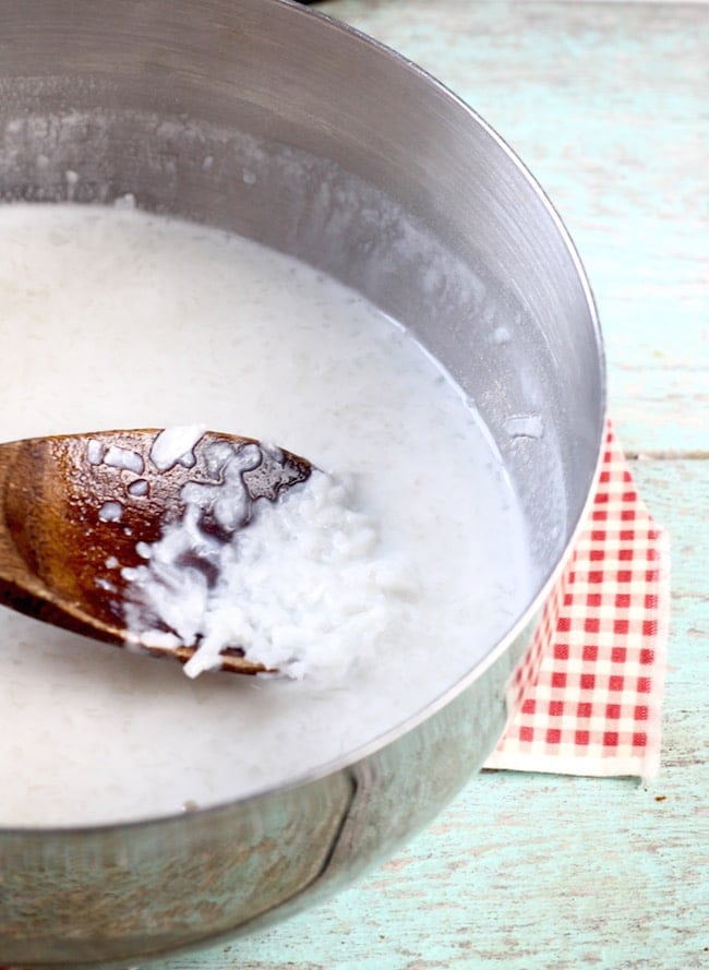 Coconut and milk mixture in a pan with a wood spoon for coconut cream cake recipe
