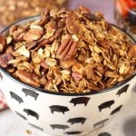 Easy granola recipe with pecans and almonds in a black and white bowl with blueberries and strawberries on the white back ground