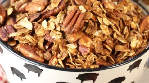 Easy granola recipe with pecans and almonds in a black and white bowl with blueberries and strawberries on the white back ground