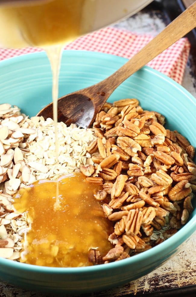 Pouring honey and oil mixture over bowl of oats, pecans and almonds