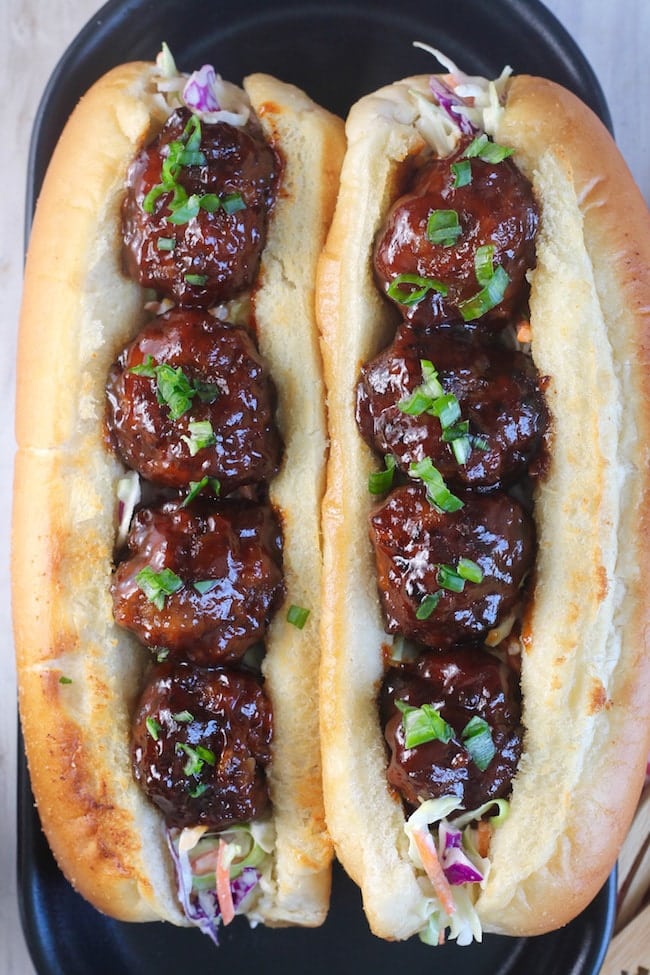 Two Barbecue Meatball Hoagie Sandwiches garnished with Green onions on a black platter